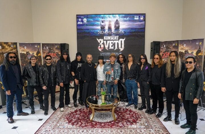 Group of musicians posing for a photo in a room with posters, a large screen, and a red rug beneath a glass coffee table.