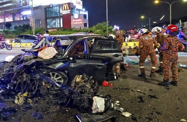 Night scene of a multi-vehicle crash: a severely damaged dark SUV with debris; firefighters in orange camouflage gear work at the site.