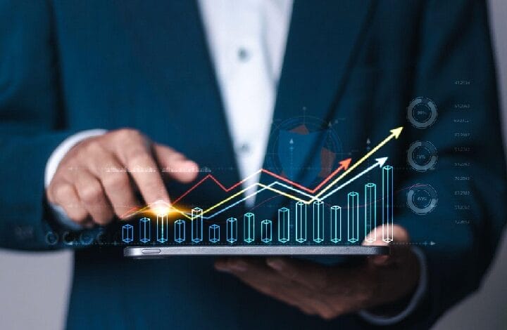 Businessperson in a suit holding a tablet displaying glowing upward-trending graphs and charts.",