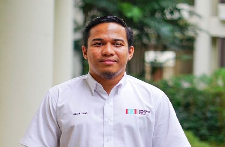 Portrait of a man in a white button-up shirt standing outdoors with greenery in the background.