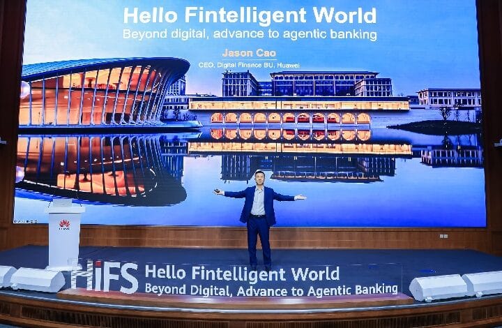 Speaker in blue suit on a stage with a large screen reading 'Hello Fintelligent World' and 'Beyond digital, advance to agentic banking' behind him.