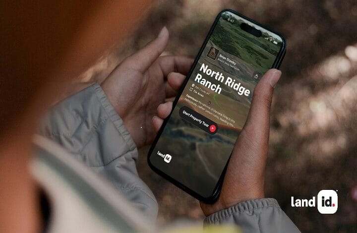 Person holding a smartphone displaying the North Ridge Ranch property page in the land id app outdoors