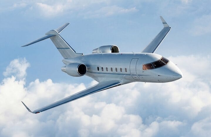 White private jet soaring above fluffy clouds in a clear blue sky, mid-flight with wings swept back for cruising speed.