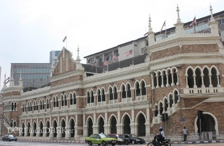 Historic brick building with white arches and balconies, US flags along the roofline, on a busy city street.