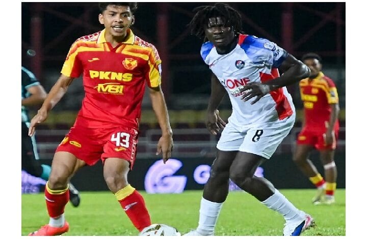 Two soccer players contest the ball on a grass field during a night match, one in a red-yellow kit and the other in white-blue, near the foreground image center.