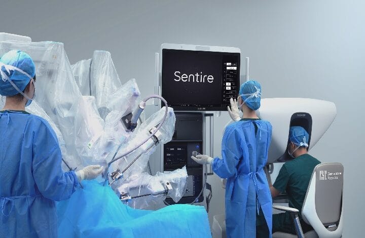 Surgeons in blue gowns operate a robotic-assisted surgery system in an operating room, monitoring a screen that reads Sentire.