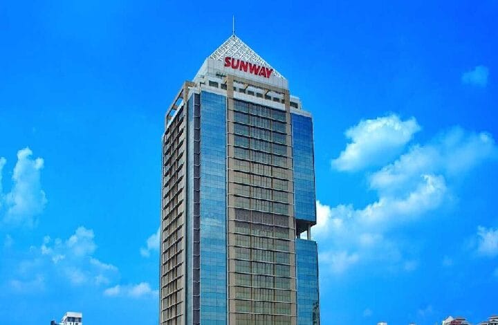 Tall glass office tower with the Sunway logo at the top against a bright blue sky