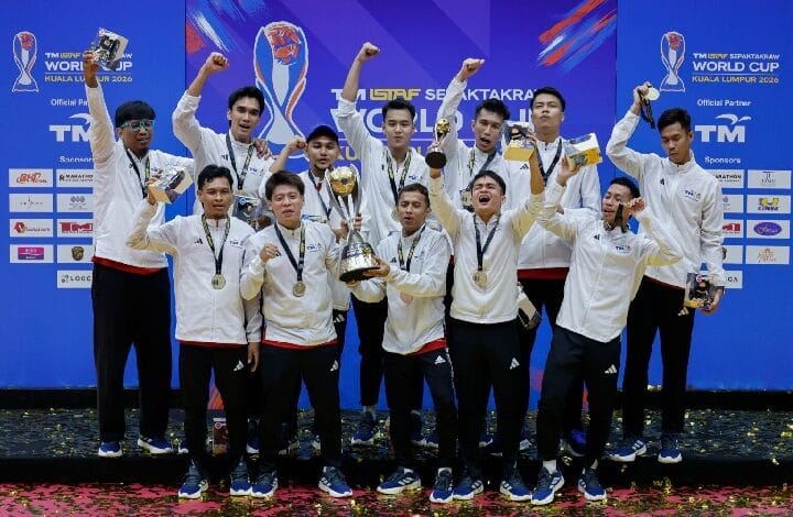 Twelve athletes in white jackets celebrate on stage with medals and a large trophy at the World Cup Kuala Lumpur 2026 backdrop.