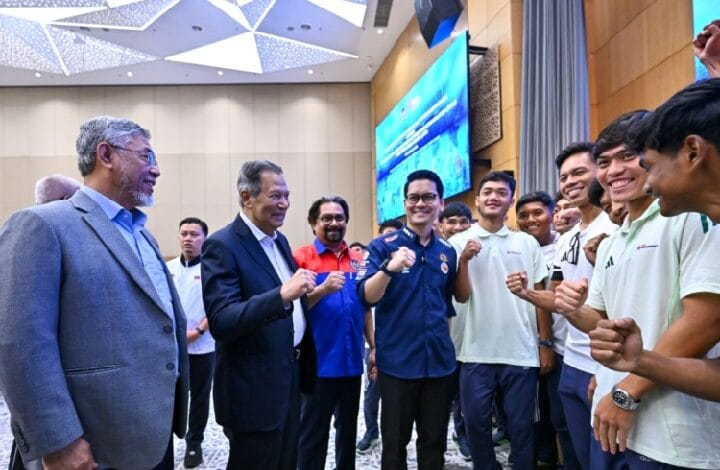 Group of men and young adults pose in a conference room, fists raised in a gesture of teamwork and unity.