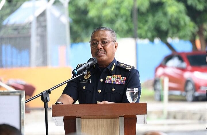 Senior military officer in dress uniform with medals delivering a speech at a wooden podium outdoors, microphone nearby and a wine glass on the lectern.