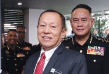 abdul halim aman - Wilayah.com.my Two men pose for a photo at a formal military event, with uniformed officers in the background, indoors.