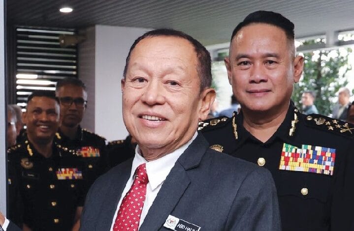 abdul halim aman - Wilayah.com.my Two men pose for a photo at a formal military event, with uniformed officers in the background, indoors.