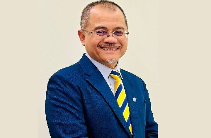 aimi zulhazmi - Wilayah.com.my Smiling man in a blue suit with a yellow and blue striped tie, standing against a light background.