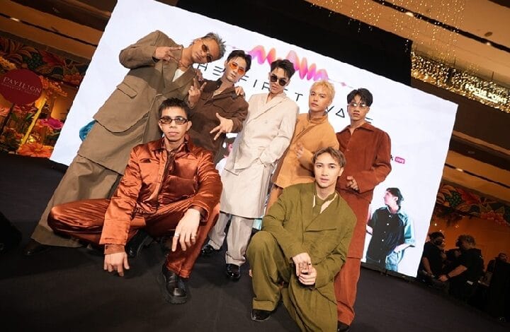 alpha mpop - Wilayah.com.my Group of eight male models posing on a fashion show runway, wearing bold, retro-colored suits with a bright screen backdrop behind them.