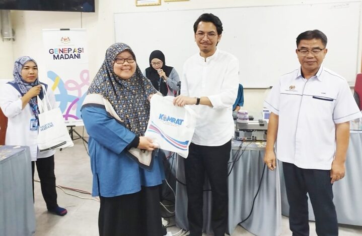 Man in a white shirt hands a branded bag to a smiling woman in a blue hijab at a community event; others look on.