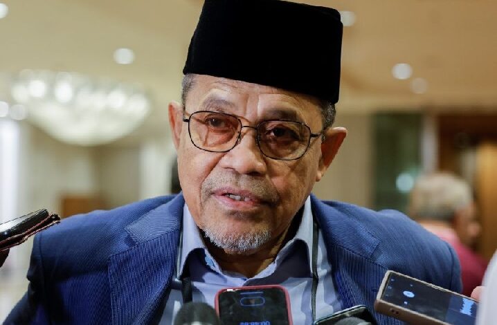 anwar japan 2 - Wilayah.com.my Portrait of a middle-aged man wearing a black traditional cap and glasses, speaking to reporters with handheld microphones nearby.
