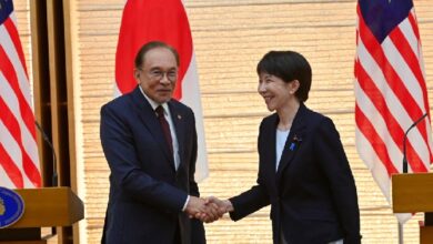 anwar japan 2 - Wilayah.com.my Diplomats from Japan and Malaysia shake hands during a formal event, with national flags in the background.
