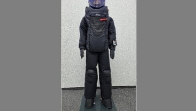 Humanoid robot in a black protective suit with a blue-lit head, standing on a mat.