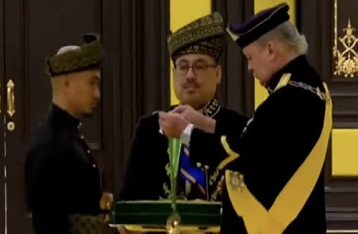 Three men in ceremonial uniforms stand in a doorway as a senior official pins a medal from a green case to another official.