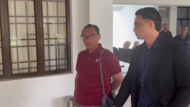azman hakim hassanuddin - Wilayah.com.my Two men walking in a bright hallway; one in a maroon polo with a shoulder bag, the other in a dark suit gesturing as they talk.