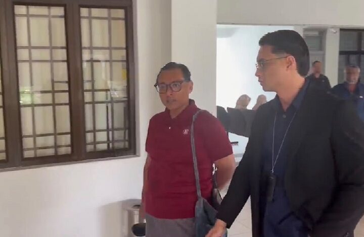 azman hakim hassanuddin - Wilayah.com.my Two men walking in a bright hallway; one in a maroon polo with a shoulder bag, the other in a dark suit gesturing as they talk.