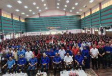 Large group photo in a big hall; front row seated officials and dozens of attendees standing behind them in blue and red outfits at an event.