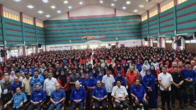 Large group photo in a big hall; front row seated officials and dozens of attendees standing behind them in blue and red outfits at an event.
