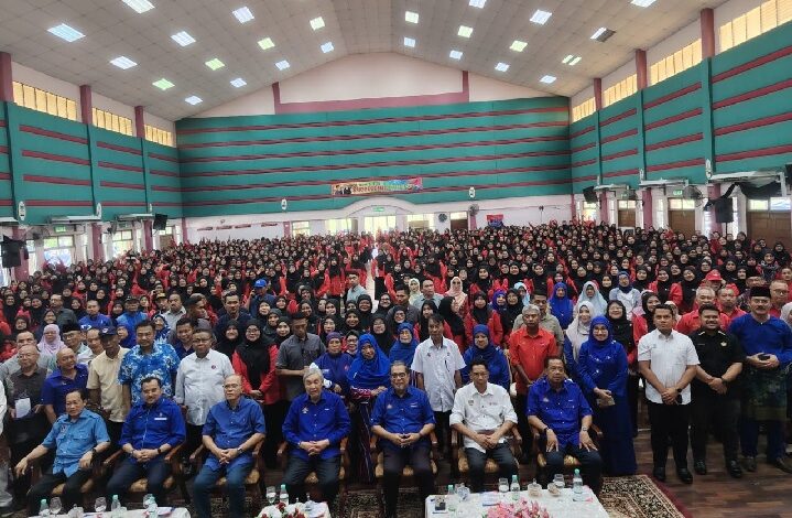 Large group photo in a big hall; front row seated officials and dozens of attendees standing behind them in blue and red outfits at an event.