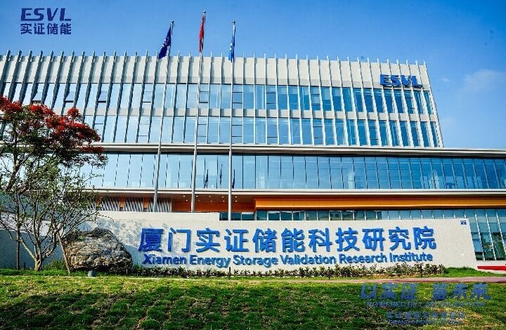 Modern glass-front building with an 'Xiamen Energy Storage Validation Research Institute' sign, ESVL logo, flagpoles, and manicured landscaping in front.