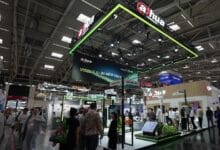 Dahua booth at a large exhibition hall with a neon-green, suspended canopy and crowd of attendees exploring security product displays on the floor below.