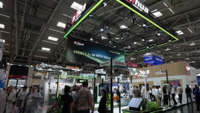 Dahua booth at a large exhibition hall with a neon-green, suspended canopy and crowd of attendees exploring security product displays on the floor below.