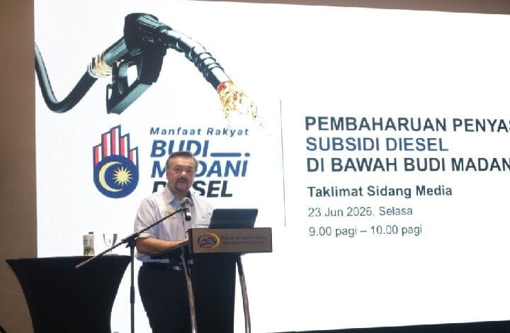 Man at a podium giving a talk, with a large presentation screen and diesel subsidy imagery in the background