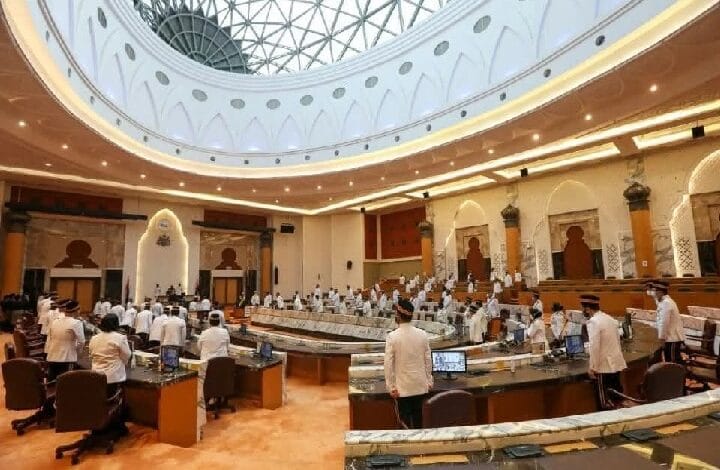 Parliamentary chamber with a large circular skylight, delegates in white shirts seated around curved desks in a grand assembly hall.