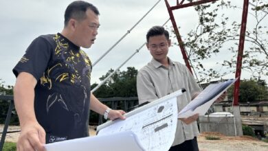 engineer - Wilayah.com.my Two men review large blueprints at an outdoor construction site, examining plans together.