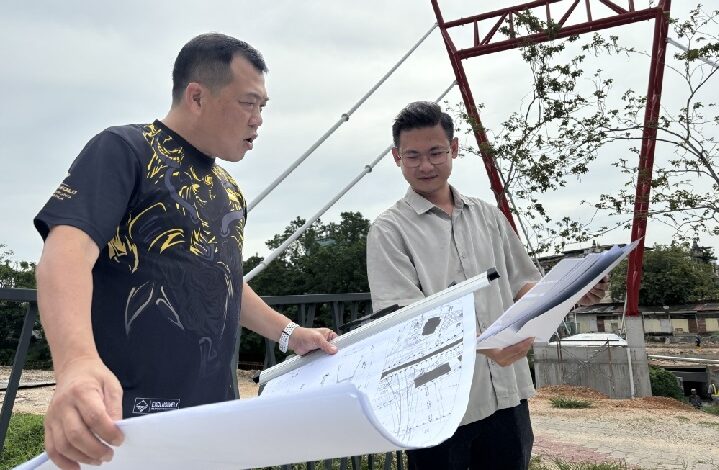engineer - Wilayah.com.my Two men review large blueprints at an outdoor construction site, examining plans together.