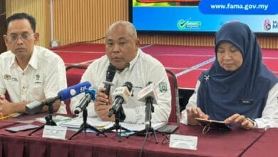 faisal iswardi 2 - Wilayah.com.my Three officials sit at a red table during a press conference; the man in the center speaks into a handheld microphone surrounded by reporters' microphones.