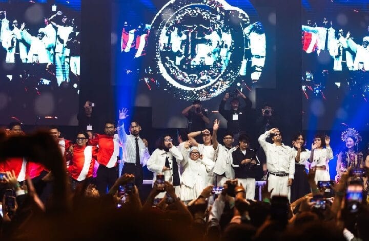 feast band - Wilayah.com.my Group of performers on a lit stage, many in white outfits, audience filming with phones; large logo on screens behind.
