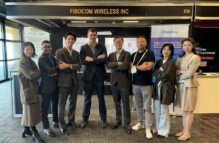 fibocom 2 - Wilayah.com.my Group of eight professionals in business attire posing with arms crossed at a Fibocom Wireless Inc booth at a tech conference.