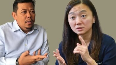 Two adults seated and talking; man on the left gestures with an open hand while the woman on the right speaks, using finger gestures to emphasize a point.