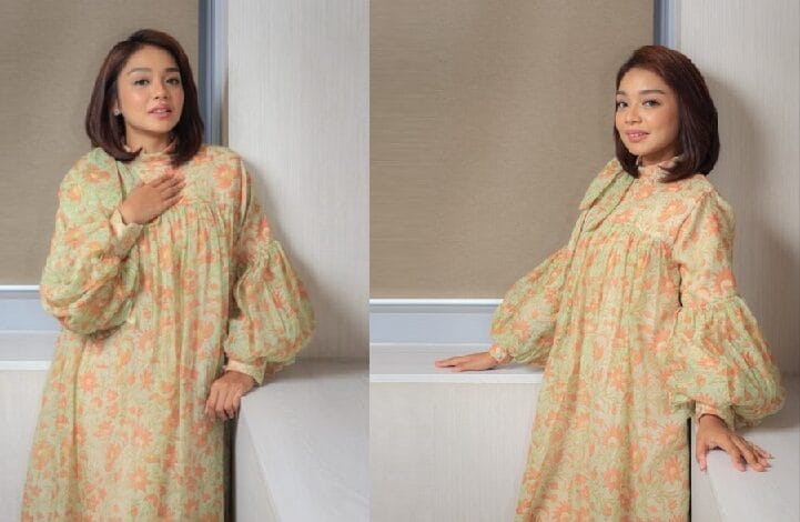 harissa adlynn 2 - Wilayah.com.my Woman in a pastel peach and mint floral dress with voluminous sleeves posing by a windowsill.