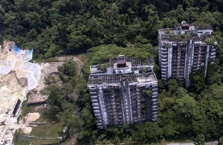 highland tower - Wilayah.com.my Two abandoned high-rise apartment blocks overtaken by dense trees in a forested area.