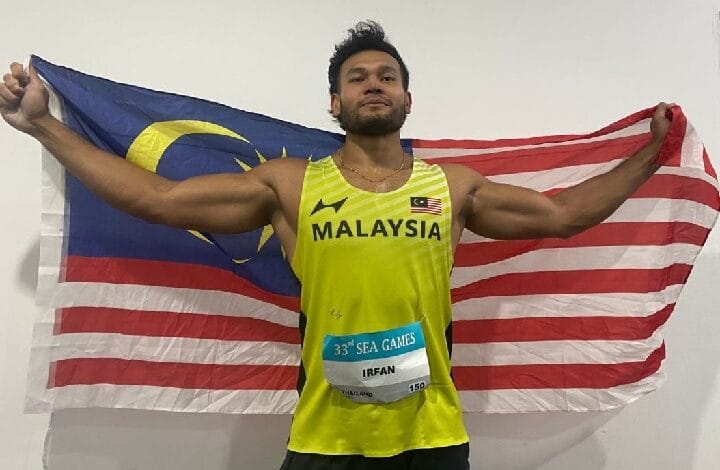 irfan - Wilayah.com.my Male Malaysian sprinter in a yellow MALAYSIA singlet, arms outstretched holding the Malaysian flag behind him; SEA Games bib reads IRFAN.