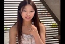 jaime tan - Wilayah.com.my Young woman with long dark hair in a white patterned sleeveless top holds a small lapel microphone toward the camera.