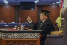 johari abdul - Wilayah.com.my Judge in a black robe and striped cap speaks from a judge's bench, gesturing with a raised finger beside a gavel and microphone.