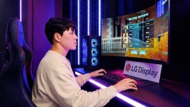 Person seated in a gaming chair at a neon-lit desk, playing a PC game on a curved monitor with an LG Display sign nearby.