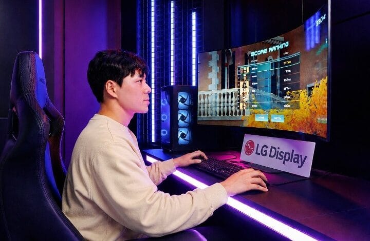 Person seated in a gaming chair at a neon-lit desk, playing a PC game on a curved monitor with an LG Display sign nearby.