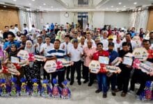Large group of people at an awards ceremony posing together, holding certificates and gift baskets.