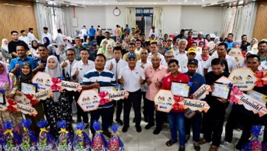 Large group of people at an awards ceremony posing together, holding certificates and gift baskets.