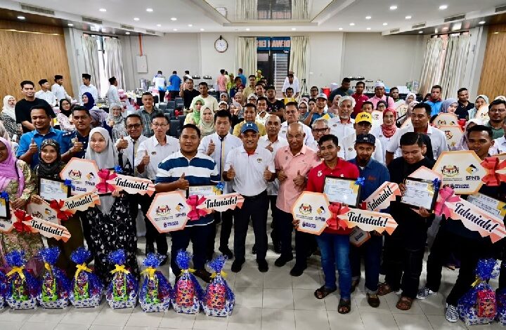 Large group of people at an awards ceremony posing together, holding certificates and gift baskets.