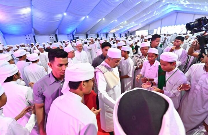 majlis tahfiz - Wilayah.com.my Large crowd of men in white traditional dress under a blue-lit tent; a cameraman records on the right.